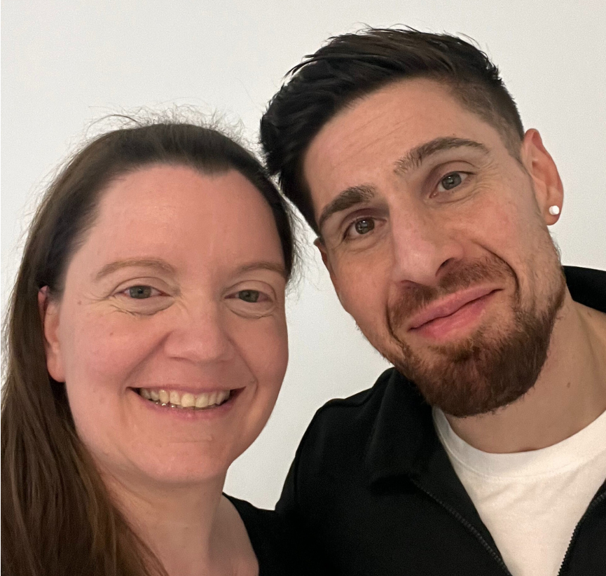 Lächelndes Paar posiert für ein Selfie vor weißem Hintergrund.